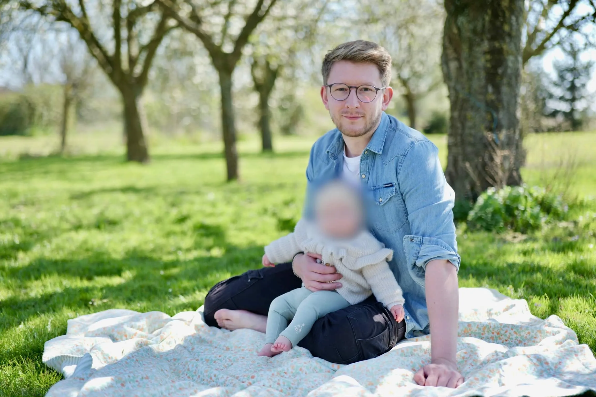 Charles Baras assis dans un verger avec sa fille sur les genoux
